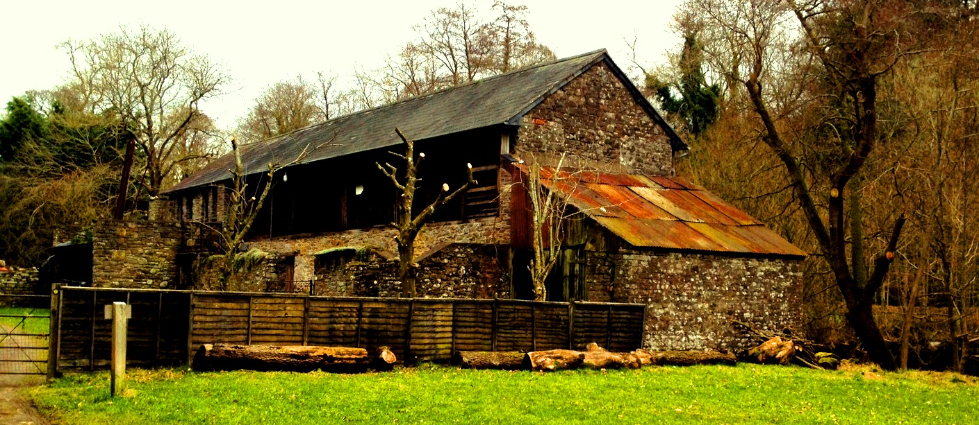 an old brick building with rusted iron roof near green grass