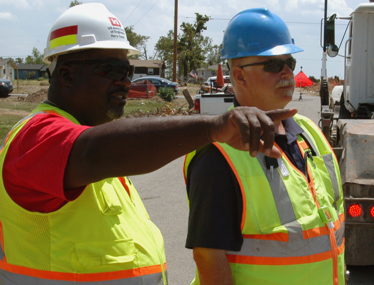 two men wearing reflective vests standing next to a truck