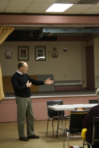 man speaking in a lecture hall surrounded by tables