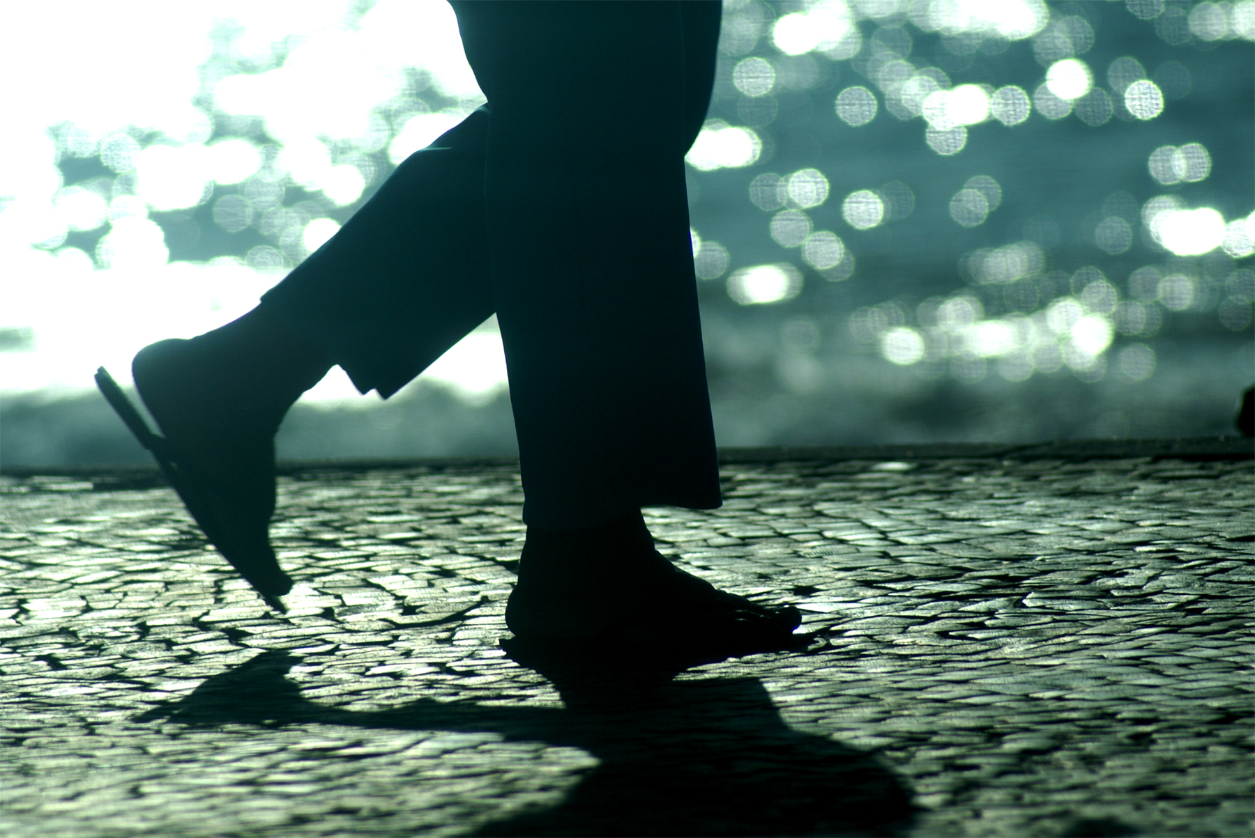 silhouette of man with black boots walking in front of rain covered street