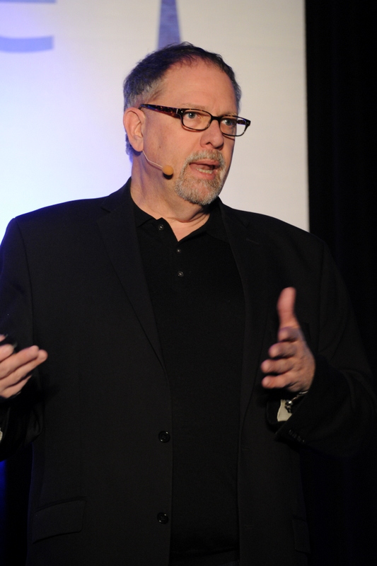 a man with a black shirt and glasses giving a speech