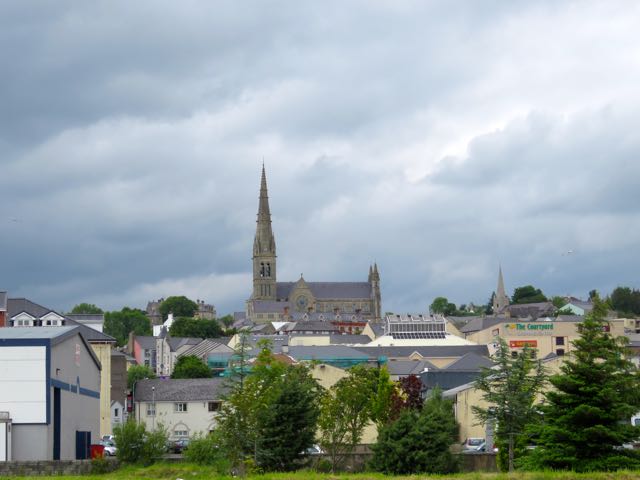 looking across a field towards some small buildings and a large church tower