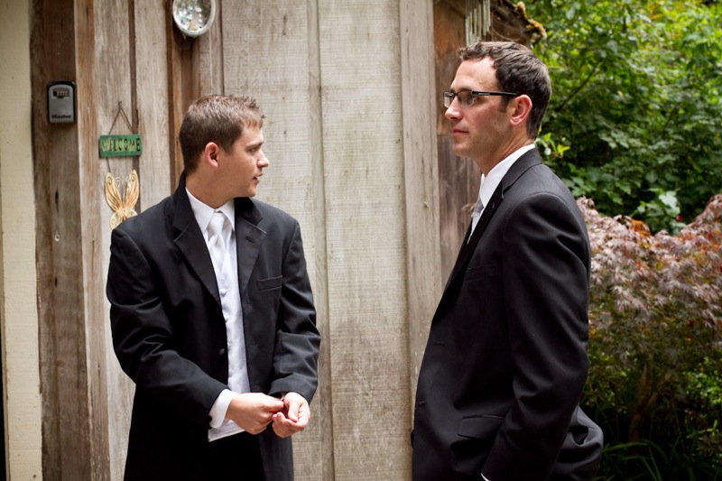 two men dressed in suits talking in front of a wooden wall