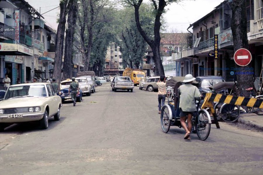 a city street with cars, motorcycles and people on the side