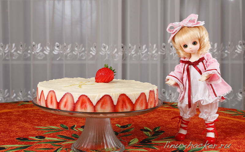 a baby doll standing next to a strawberry cake