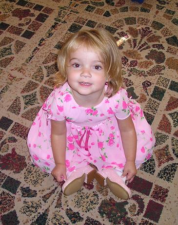 a baby girl in a pink dress is sitting on the ground