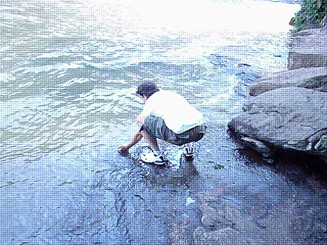a man standing in the middle of a stream holding a pair of shoes