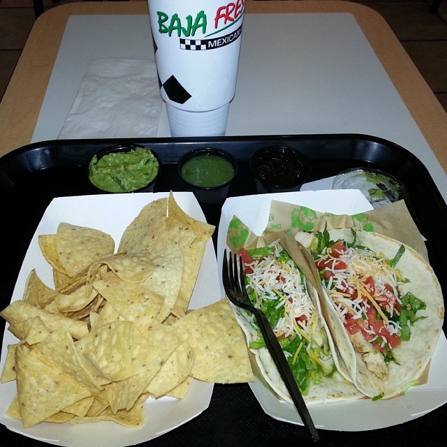 a tray topped with tacos and nachos and a drink