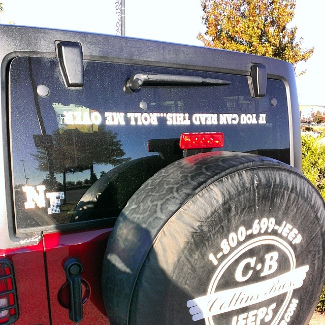 a tire with a sticker on it sits next to a red jeep