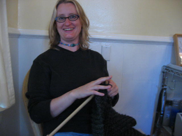 a woman sits in her kitchen while knitting