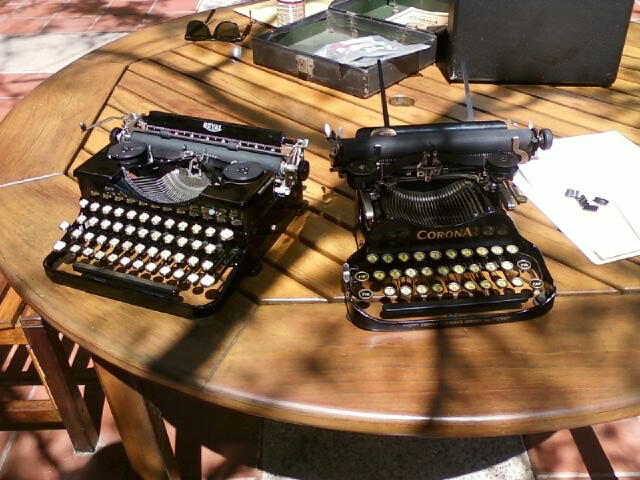 two antique typewriters sitting on a table next to a laptop