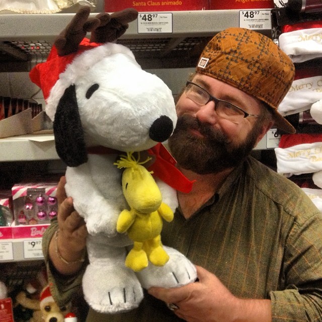 man holding up a stuffed dog and wearing a hat