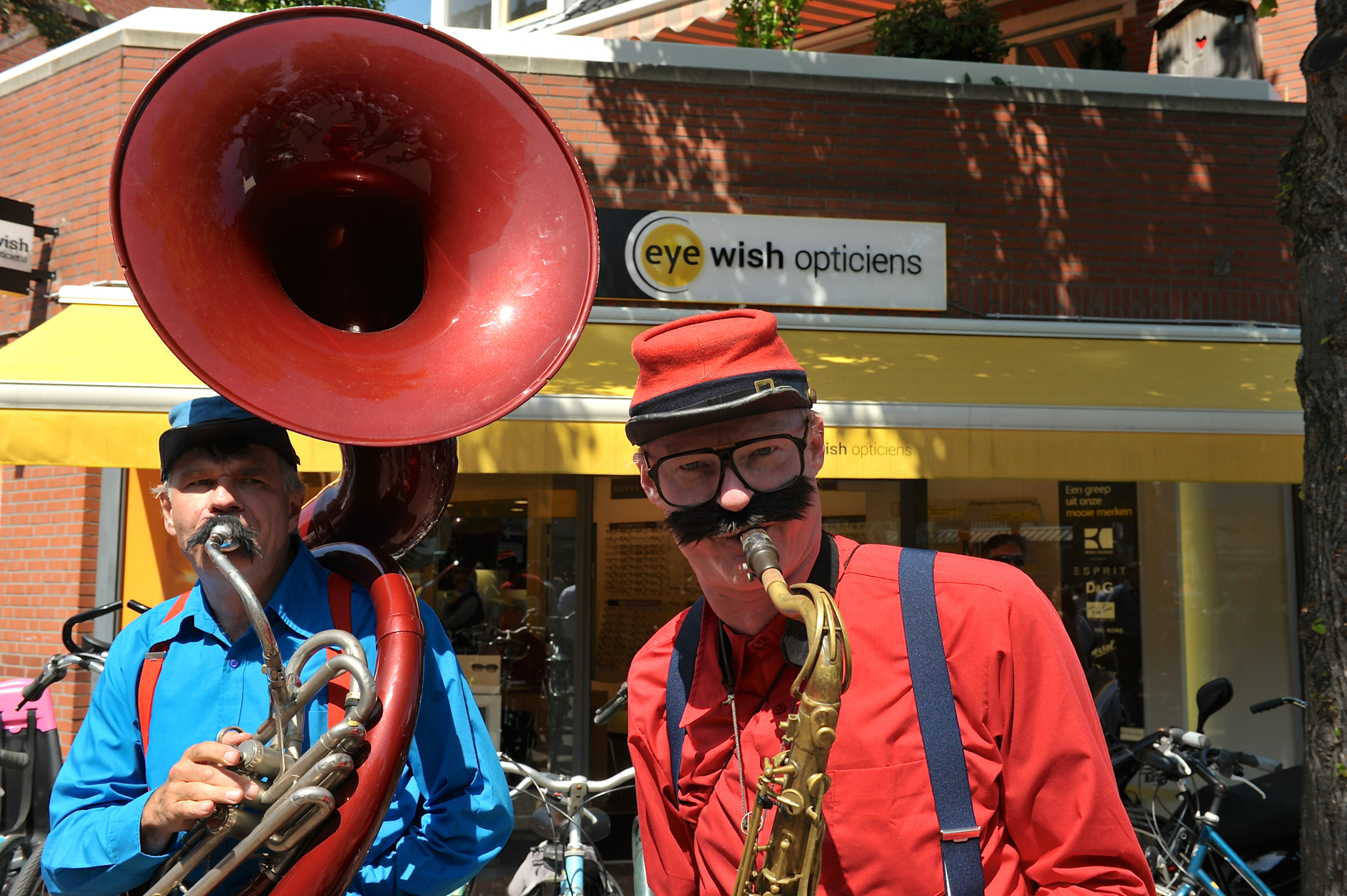 three people standing together, wearing blue shirts and red hats, playing trumpets