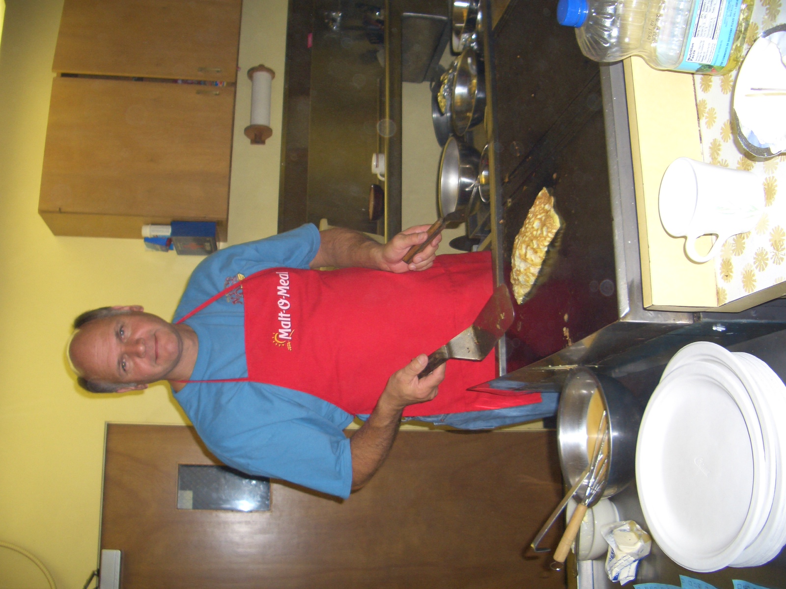 man in red apron holding onto the bottom portion of a pizza