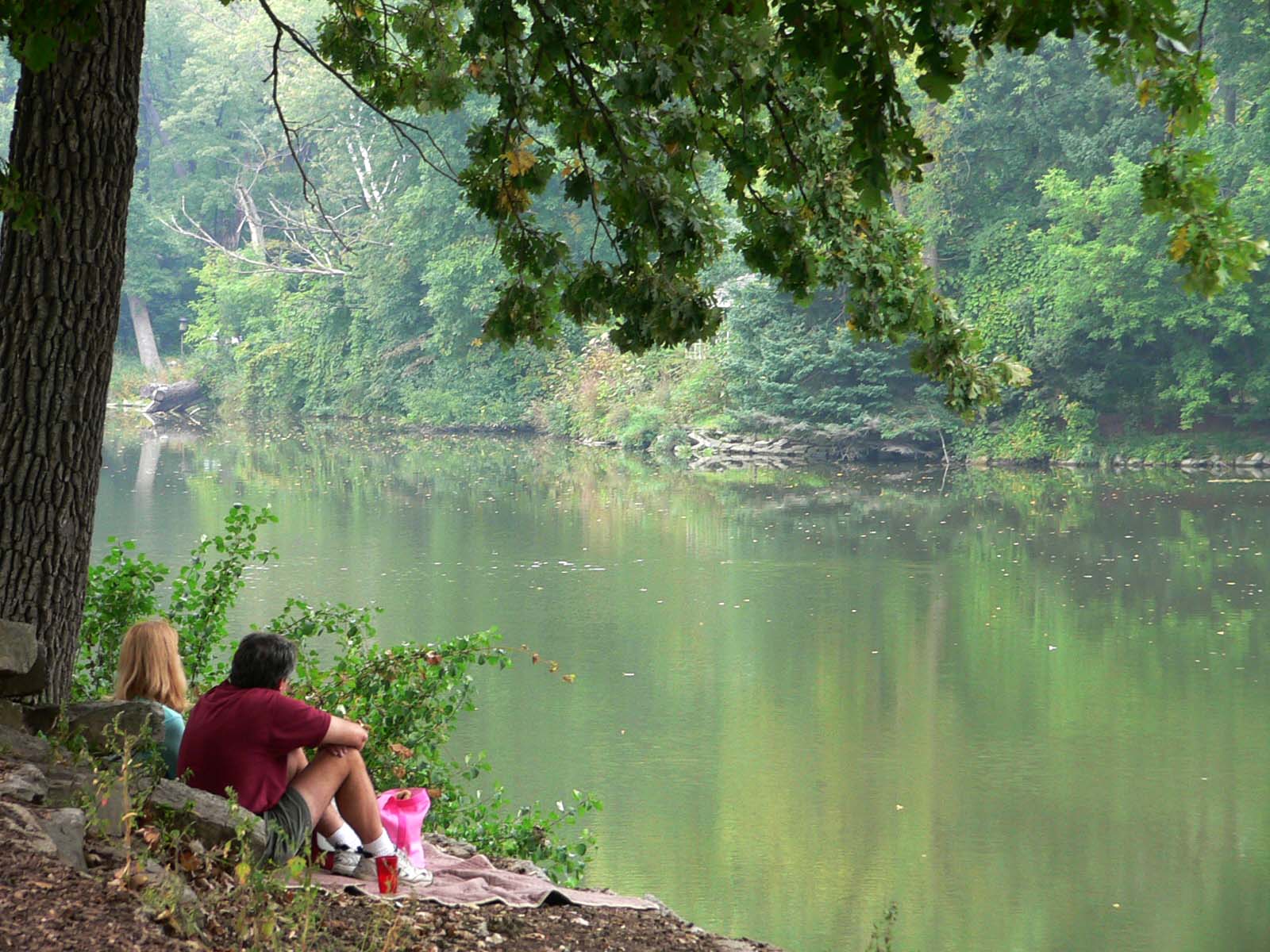 two people sitting on the end of a bench next to a lake