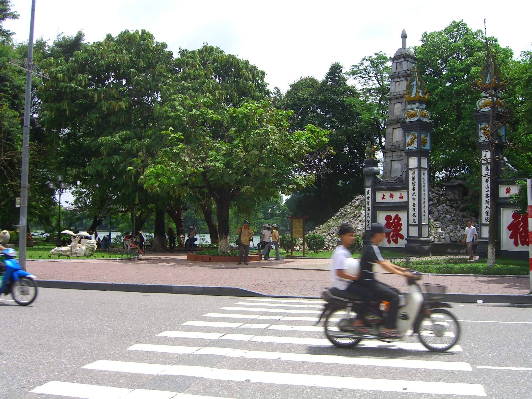 a man riding a motorcycle down a street near a tall clock