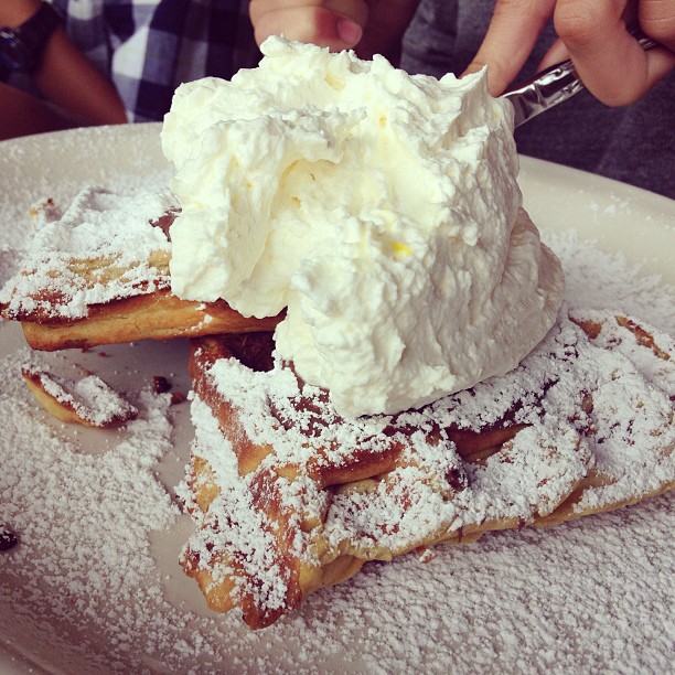 a person is scooping some cream from a waffle on top of powdered sugar