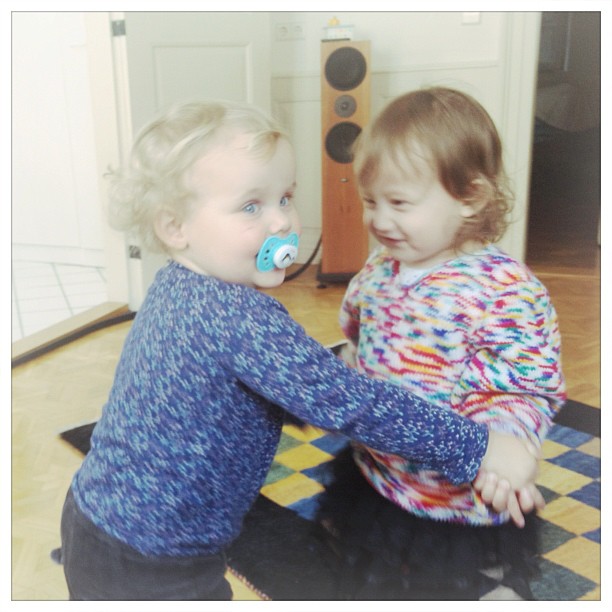 two toddlers sitting on a mat near a doorway with their pacifier