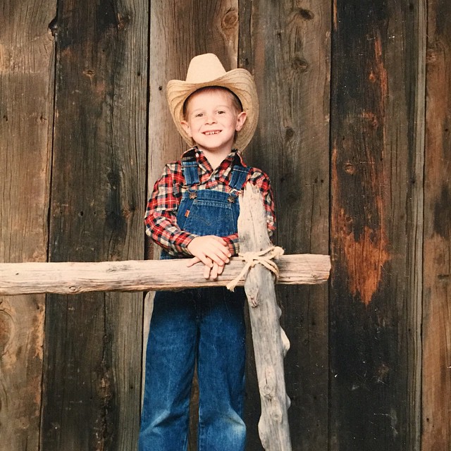 a small  in a hat holding on to a tree log