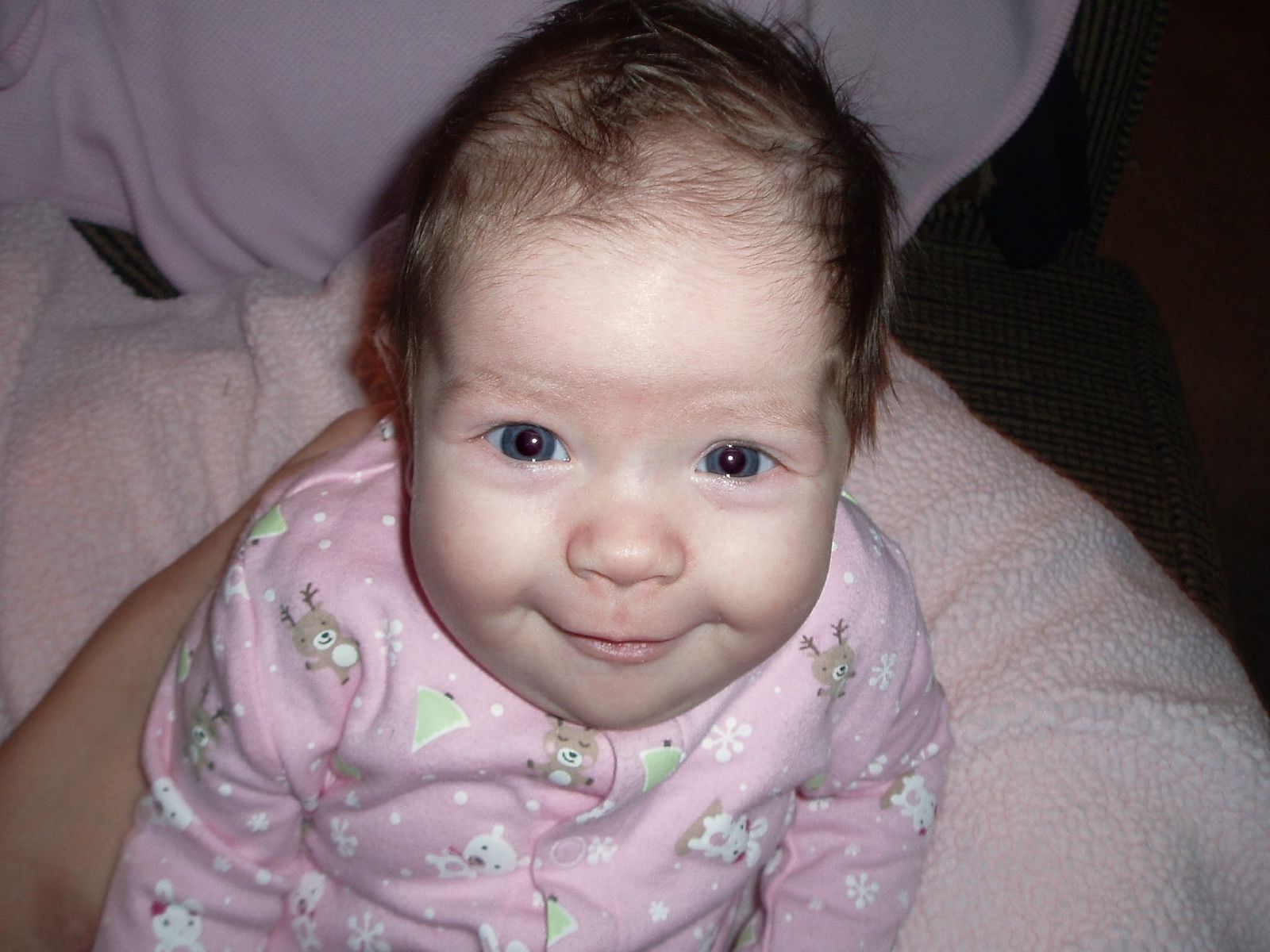 a baby with large blue eyes and pink pajamas is smiling