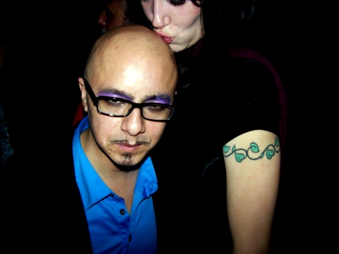 a bald man wearing glasses is next to a tattooed woman