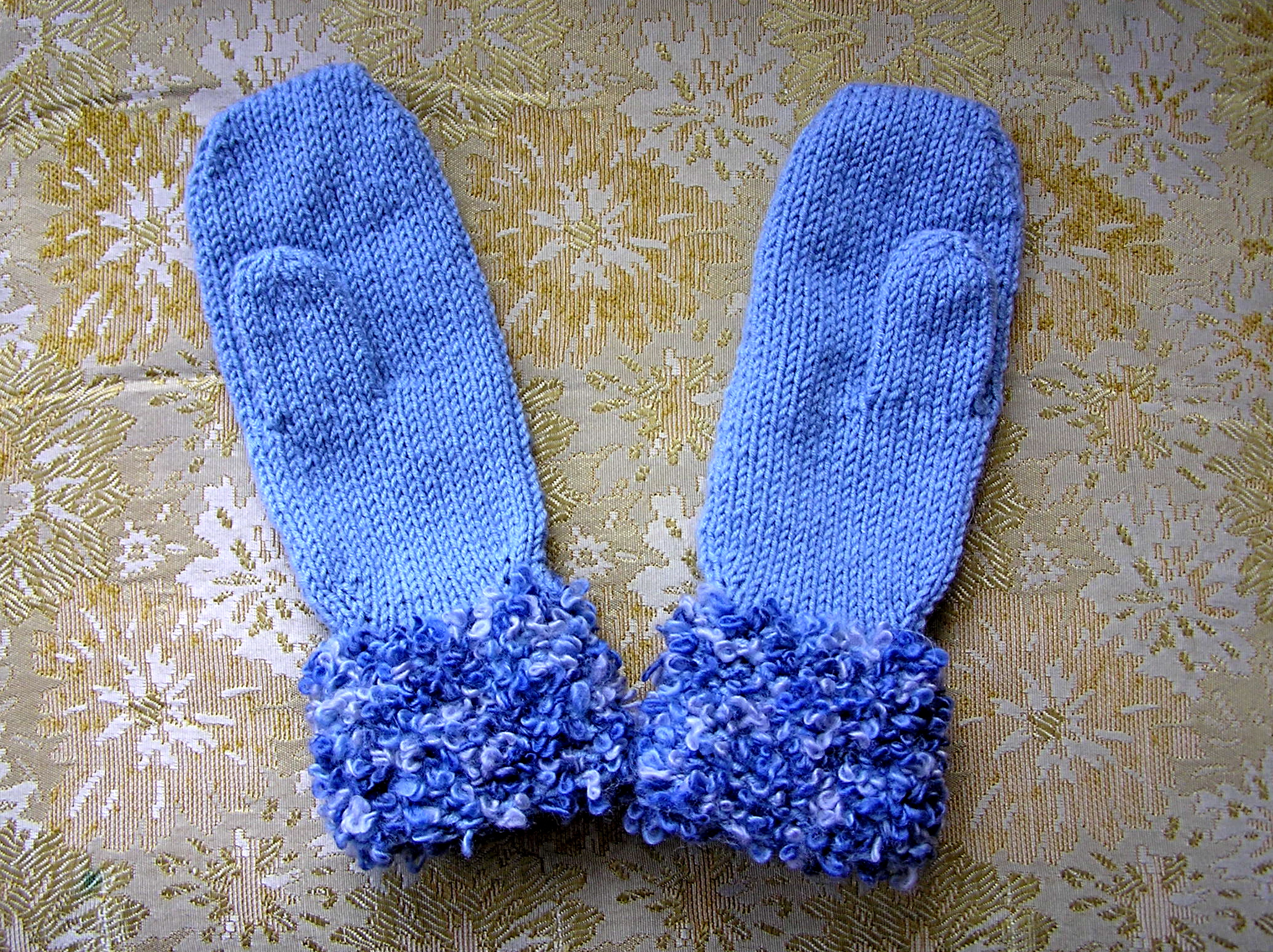 a handmade mitten with blue fur lined on a gold cloth
