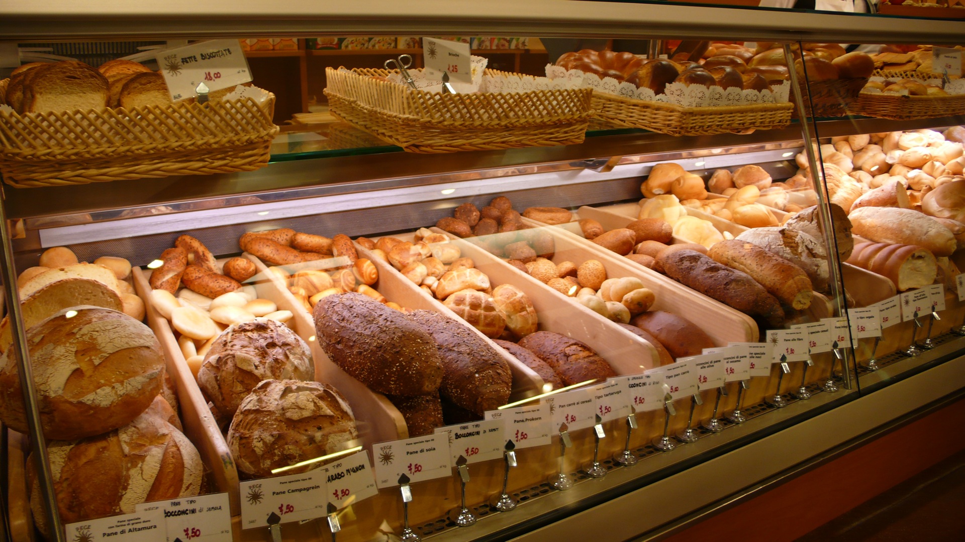 a variety of breads are behind glass in a bakery