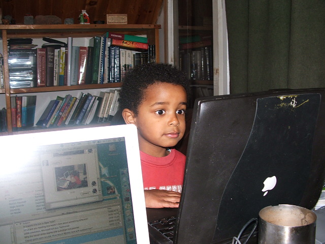small child with computer sitting near bookshelf