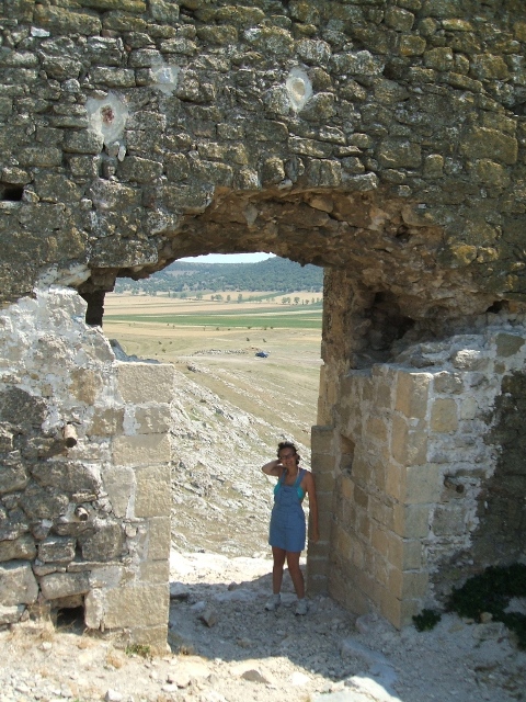 a woman posing in front of an old ruin at the bottom of a hill