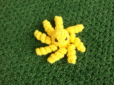 a yellow crocheted animal laying on green grass