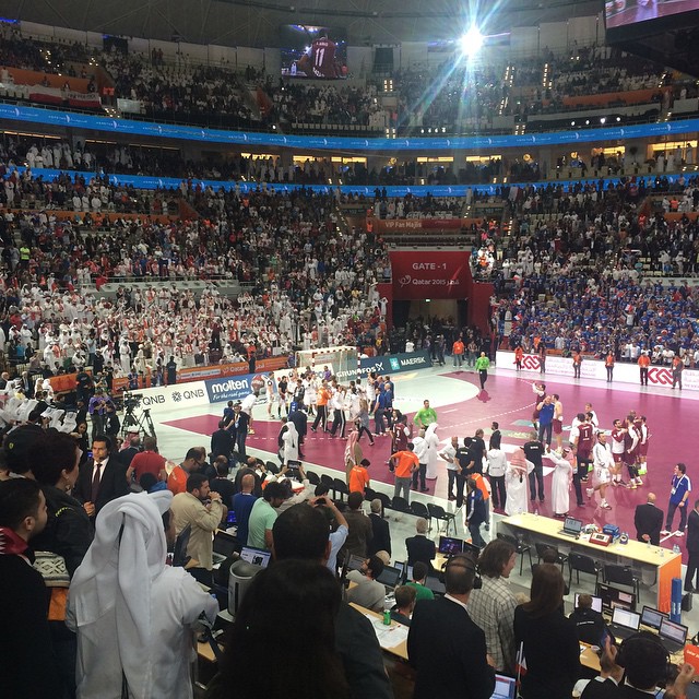 a large crowd is standing on a pink carpet in front of the large arena