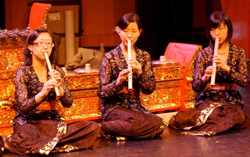 three ladies in traditional japanese costume sit on the floor with their hands near a small drum