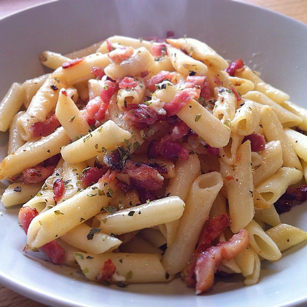 a plate filled with bacon and pasta on top of a wooden table