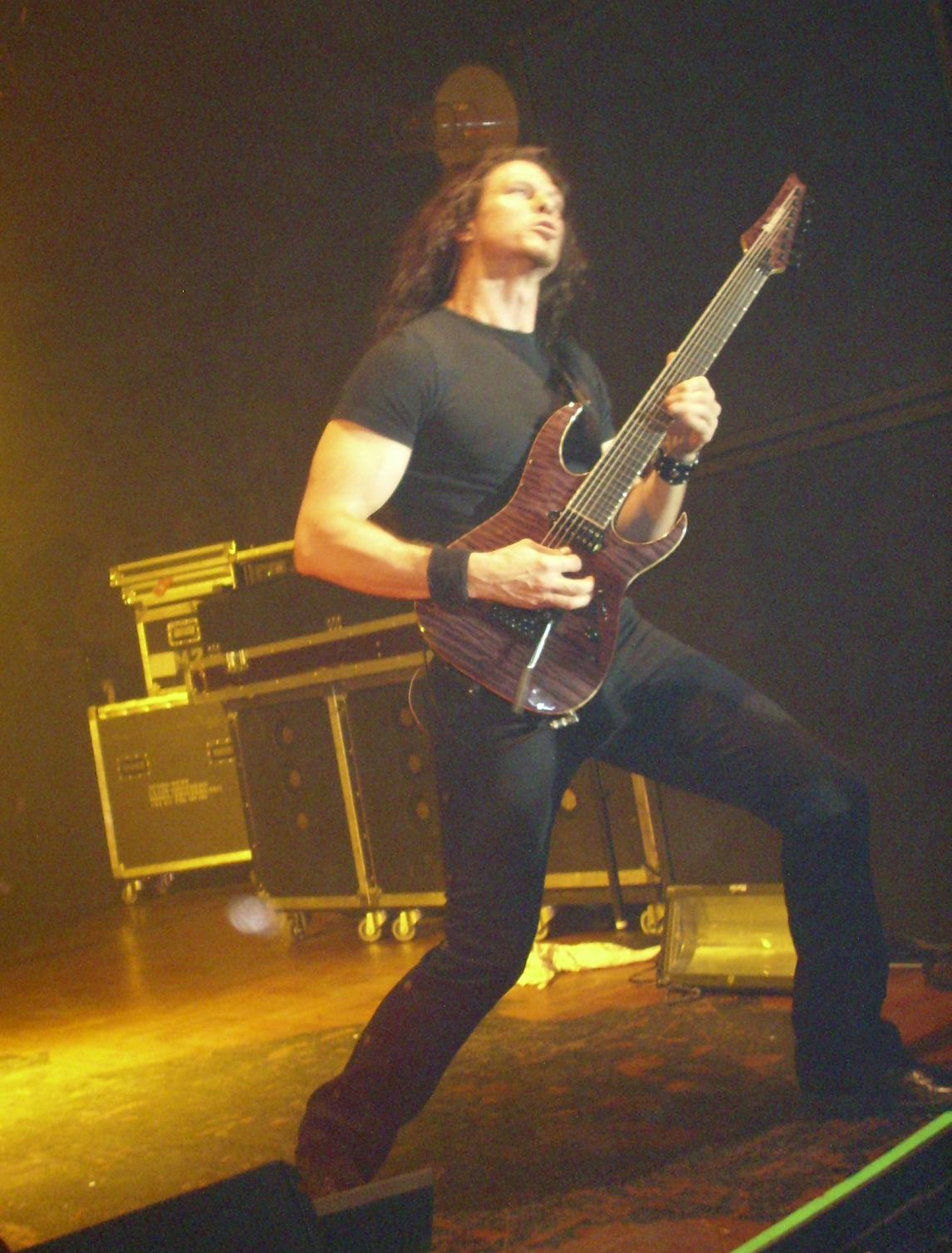 a man with long hair, holding an electric guitar on stage
