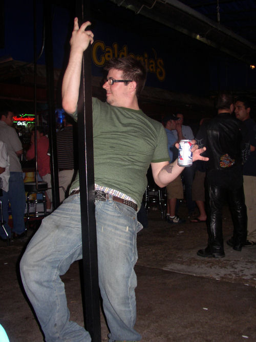 a man leaning against the side of a pole holding a cup