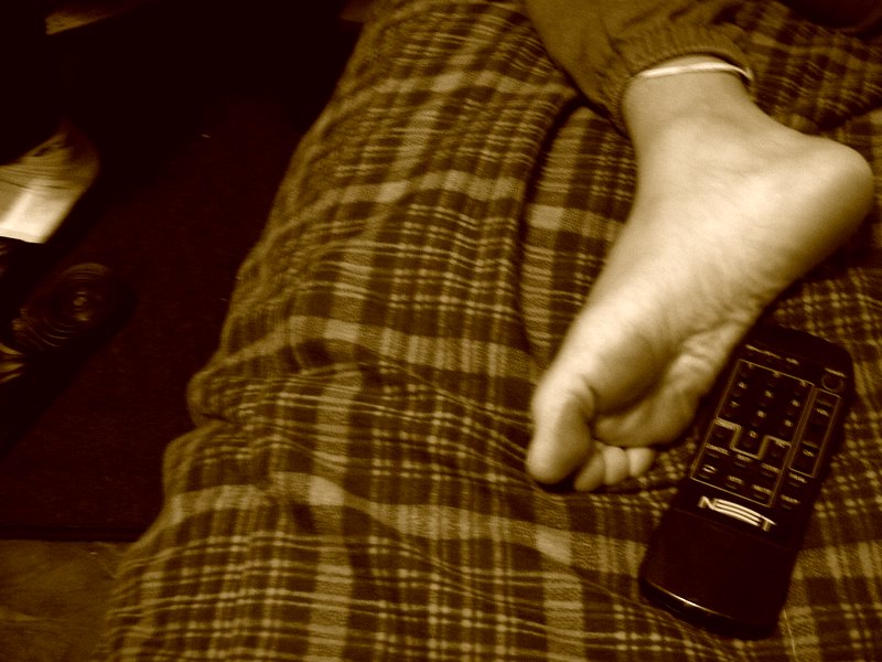a person holding onto a remote control lying on top of a bed