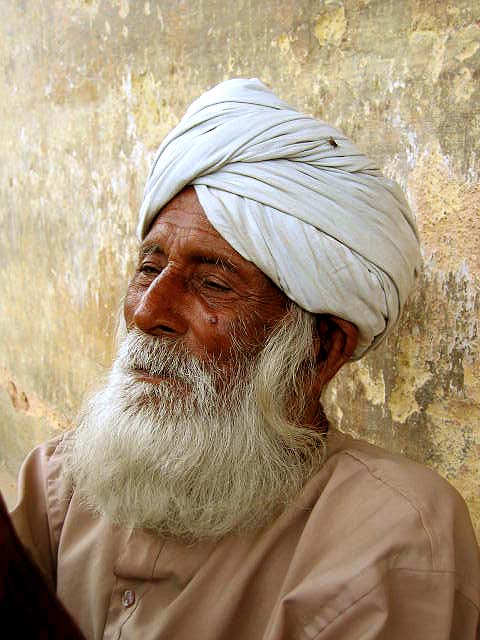 a man with a large beard wearing a turban standing next to a wall
