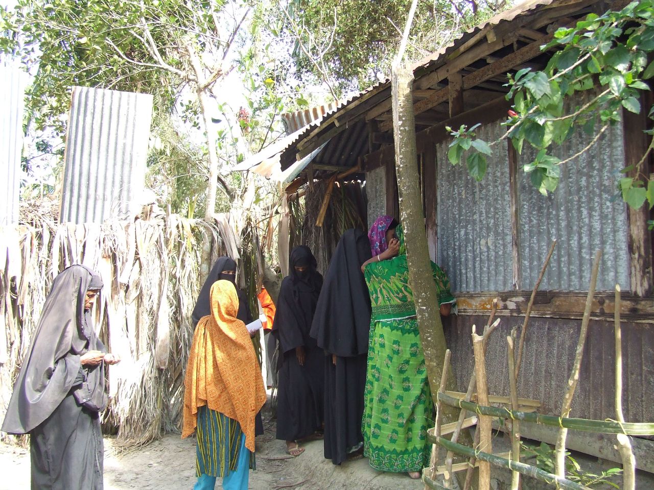 women in colorful dresses standing outside of shack