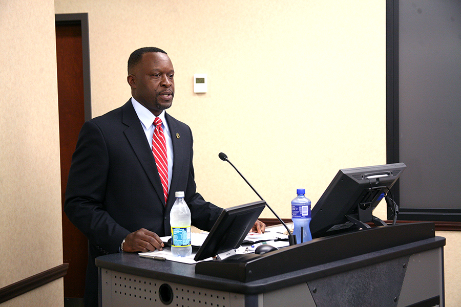 a man with a red tie standing at a podium while using a laptop