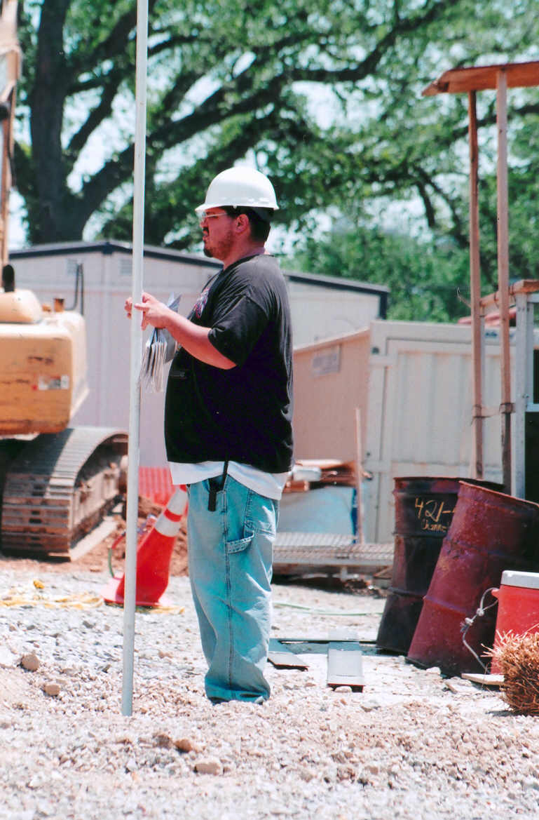 a man wearing hard hat leaning up against a pole
