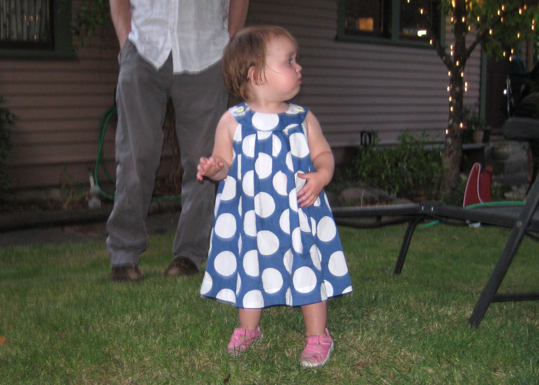 a small girl stands in the grass with her parents