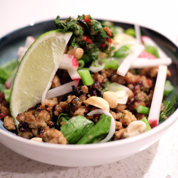 a salad with meat, onions, and greens in a bowl