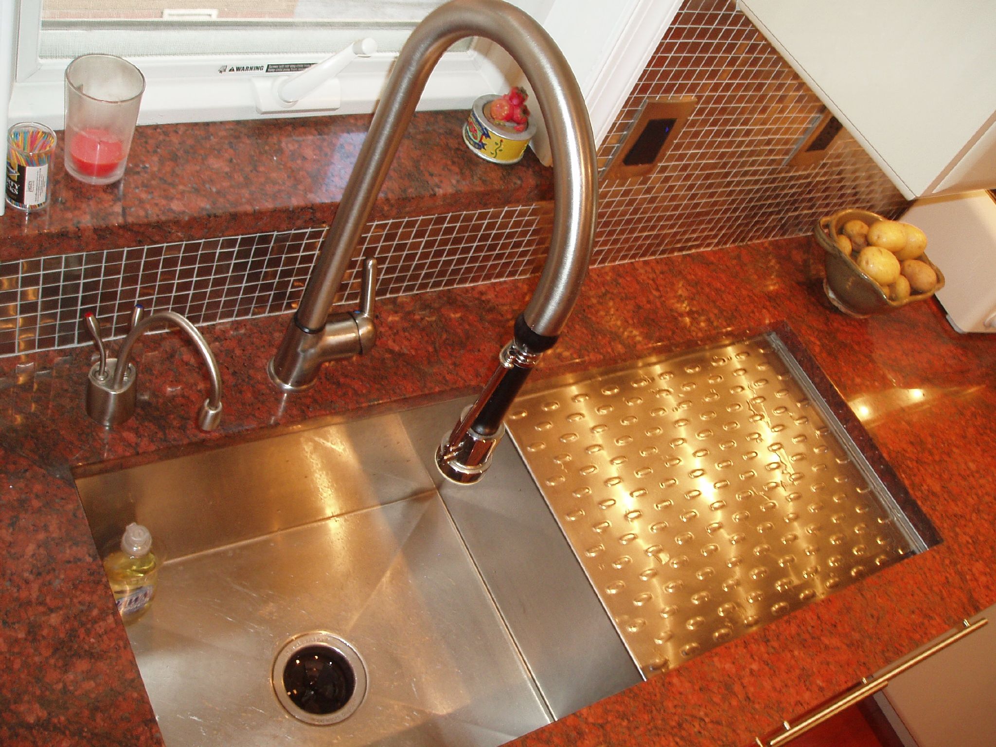 a stainless steel sink and a faucet in a small red tiled kitchen