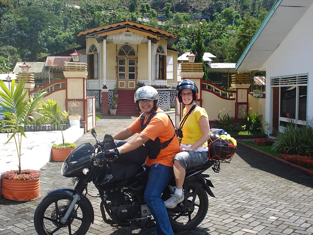 two people on a motorcycle parked outside a house