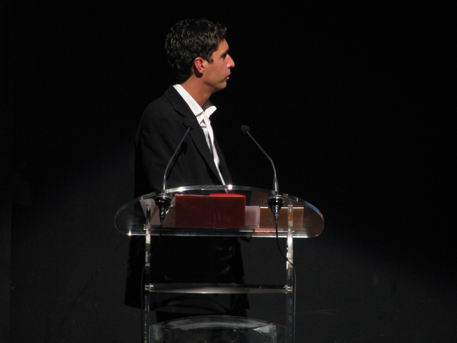a man speaking from a podium in front of a dark background
