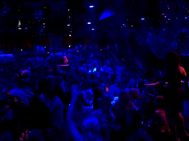 a group of people are dancing in a dark blue lit room