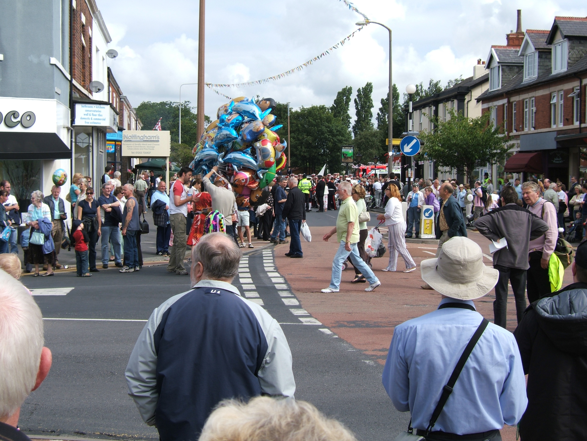 several large balloons float in the air while people walk on the sidewalk