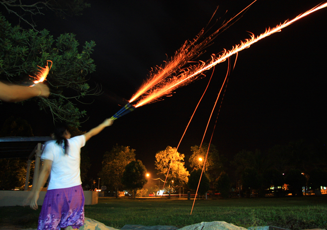 woman is flying firecrouse on night with long poles