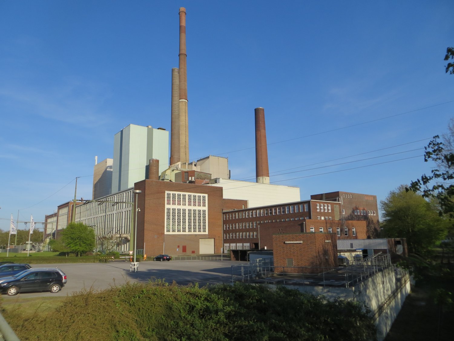 cars driving past a factory with a huge power plant