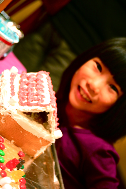 a small girl smiles next to a gingerbread house